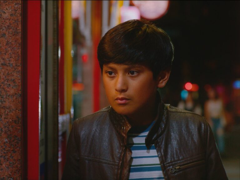 Fotograma de la película 'El tren fluvial' mostrando al niño protagonista, Milo Barria, en un entorno que mezcla lo rural y lo urbano.