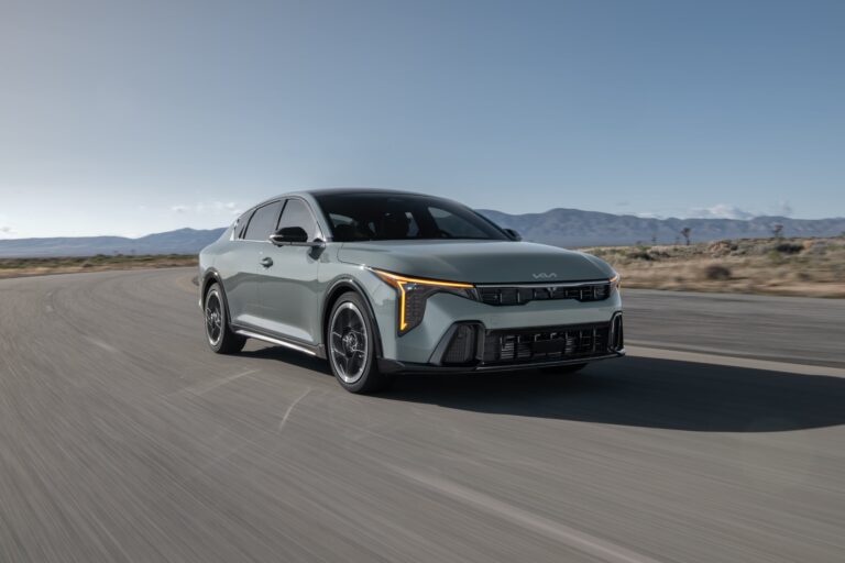 Nuevo sedán Kia K4 de color gris, con diseño aerodinámico y frontal moderno, estacionado en una calle urbana.