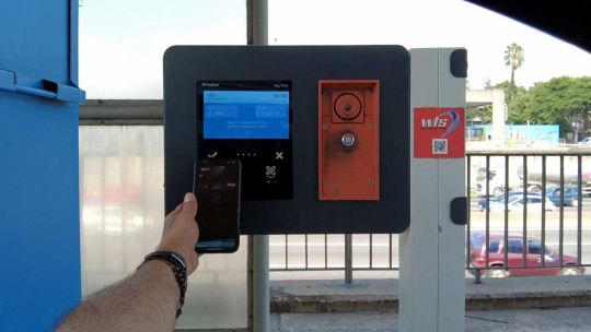 Conductor pagando peaje acercando una tarjeta a un lector contactless en una cabina de ruta.
