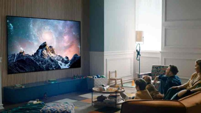 Persona sosteniendo control remoto frente a un televisor inteligente con menú de configuración en pantalla.