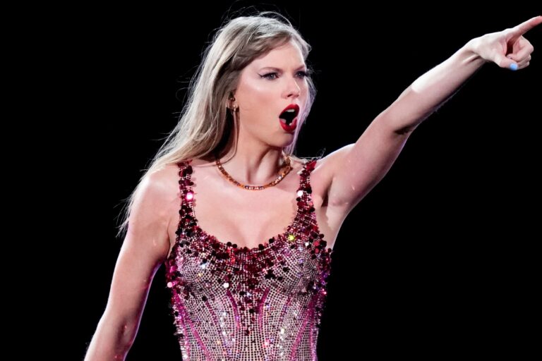Taylor Swift sosteniendo una guitarra rosa en un escenario con luces púrpuras