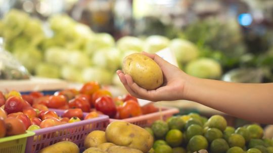 Persona haciendo compras en un supermercado de Buenos Aires, con estantes de frutas y verduras de fondo