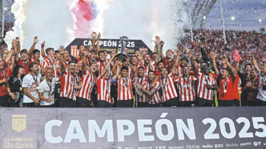 Partido de fútbol argentino con jugadores disputando el balón y banderas de la AFA de fondo