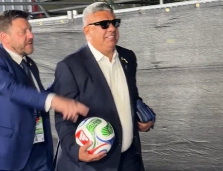 Claudio Chiqui Tapia caminando por pasillo del estadio con pelota y lentes negros