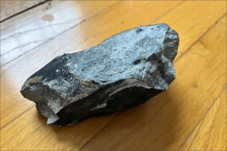 Fragmento de meteorito sobre una superficie oscura con restos de polvo negro